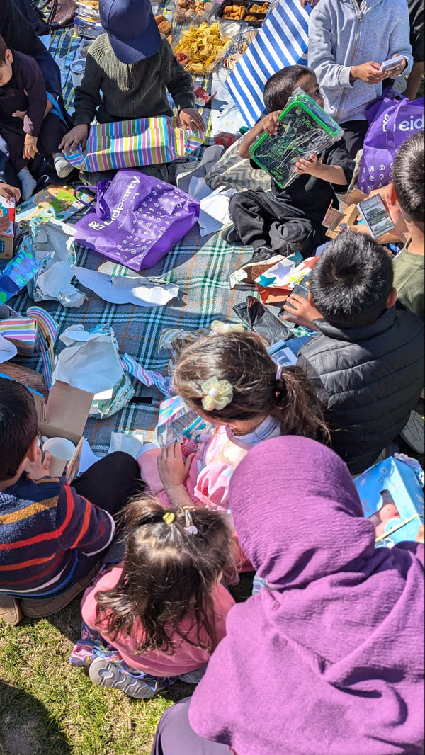 Group of people sitting on the grass with food and bags