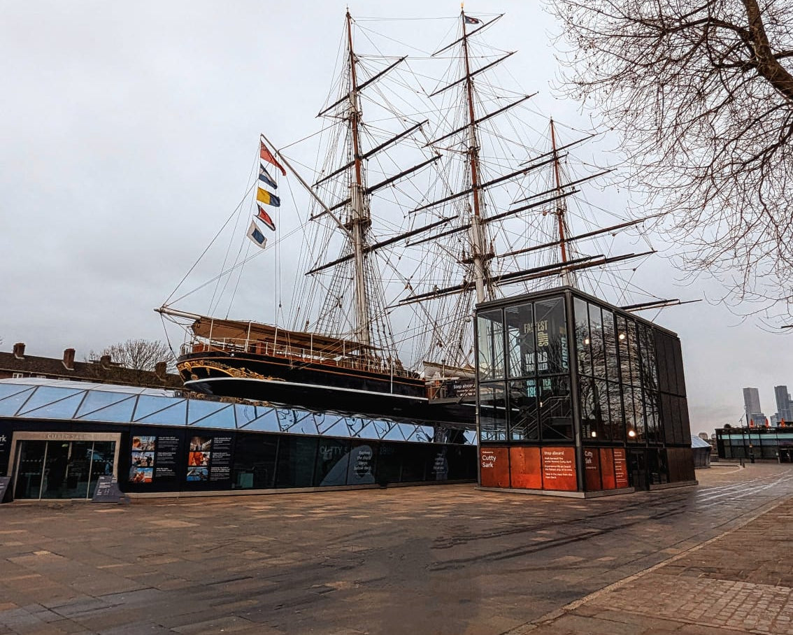 Sailing ship docked at a pier with a building in the foreground on a cloudy day.