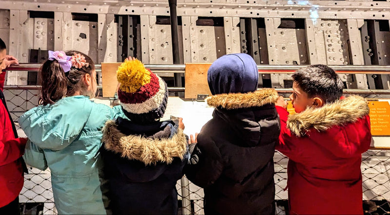 Children in winter coats looking at a digital display on a wall.