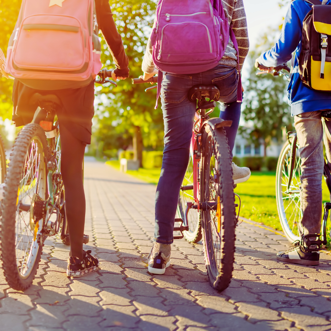 Three people riding bicycles on a paved path with backpacks.