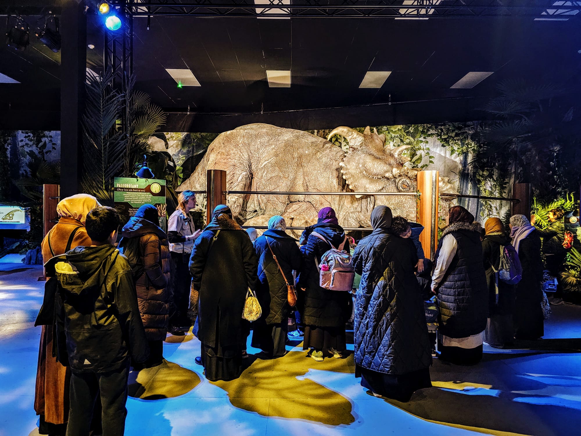 Group of people observing a large dinosaur model in an indoor exhibit.