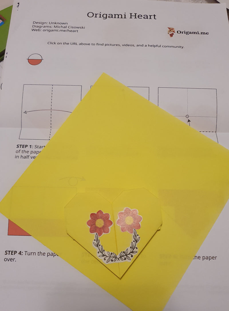 Yellow origami heart with floral design on a white background with origami instructions.