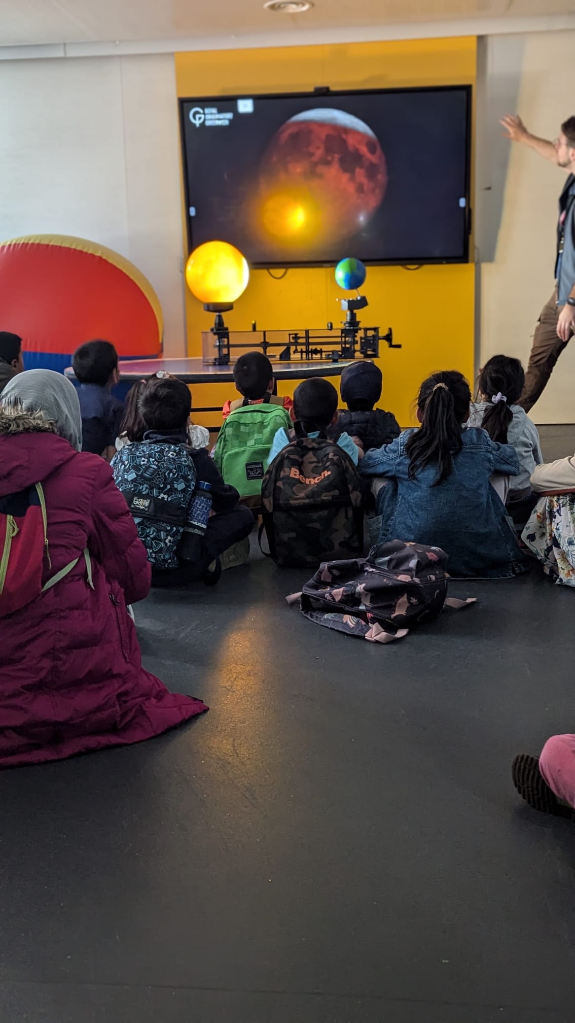 Children watching a presentation on a screen about space, with a teacher guiding them.