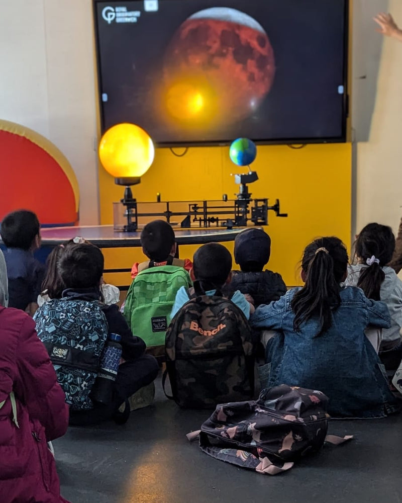 Children watching a science presentation on a screen with educational models.