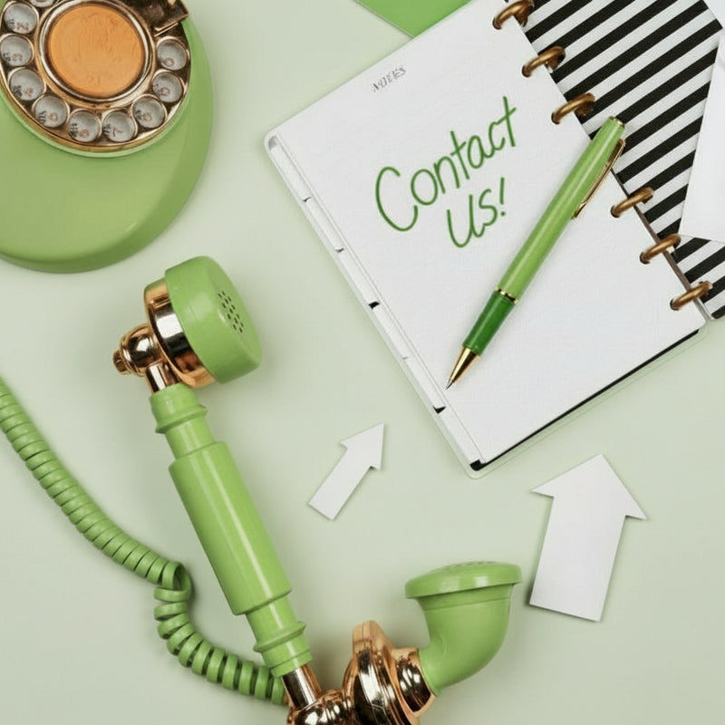Green and gold retro phone on a desk with a notebook labeled 'Contact Us!' and stationery items.